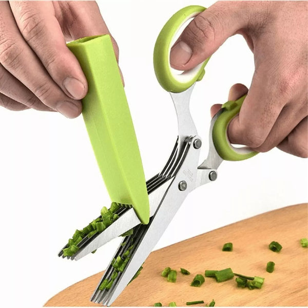 Green kitchen shears being used to chop green vegetables on a wooden cutting board.